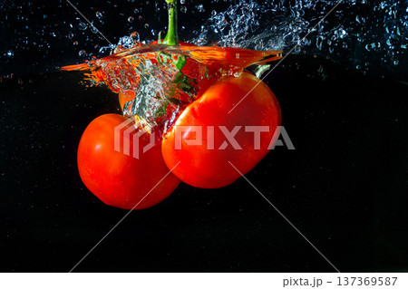 Fresh red tomato falling into water with water splash and air bubbles isolated on black background 137369587