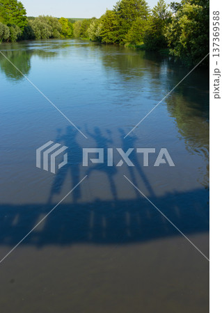 Friends enjoying a sunny day by the river, casting playful shadows on the water's surface 137369588