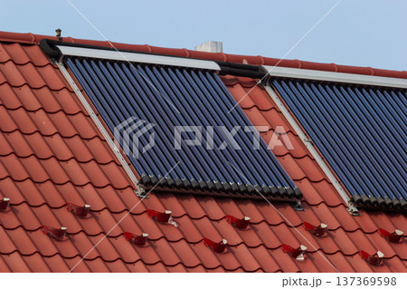 Solar thermal collectors installed on a red-tiled roof in a sunny environment promoting renewable energy use 137369598