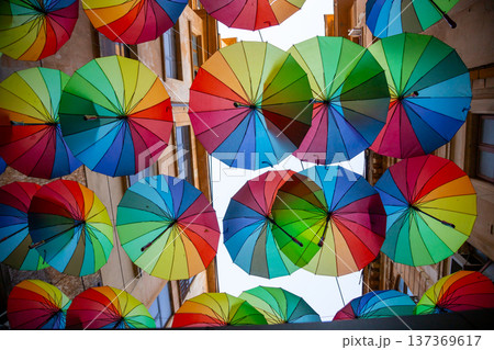 Colorful umbrellas suspended above a charming street create a vibrant and cheerful atmosphere in the heart of a lively town Colorful umbrellas suspended above a charming street create a vibrant and cheerful atmosphere in the heart of a lively town 137369617