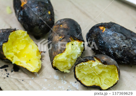 Grilled sweet potatoes served on a rustic wooden surface with a focus on their charred skin and fluffy interior 137369629