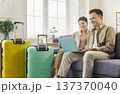 Happy couple planning vacation online at home with suitcases, booking via laptop 137370040