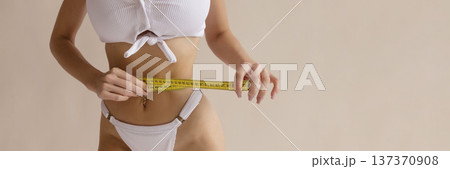 Sexy fitness diet concept with woman measuring slim waist with tape measure in white lingerie, weight loss and healthy body lifestyle Sexy fitness diet concept with woman measuring slim waist with tape measure in white lingerie, weight loss and healthy body lifestyle 137370908