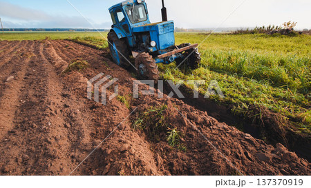 Blue tractor plowing the field creating furrows in the soil Blue tractor plowing the field creating furrows in the soil 137370919