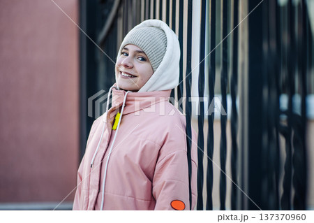 Cheerful young woman wearing a pink puffer jacket and beanie, posing outdoors 137370960