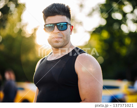 Confident man wearing sunglasses and black tank top standing outdoors at sunset Confident man wearing sunglasses and black tank top standing outdoors at sunset 137371021