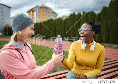 Diverse friends laughing and sharing water on sports track Diverse friends laughing and sharing water on sports track 137371379
