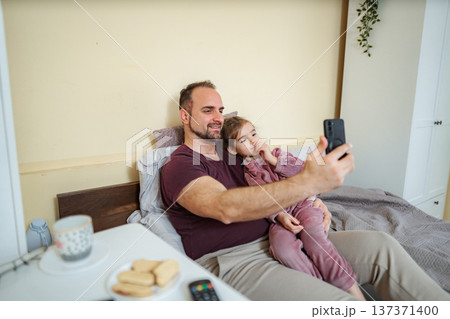 Father daughter making video call together in bed Father daughter making video call together in bed 137371400