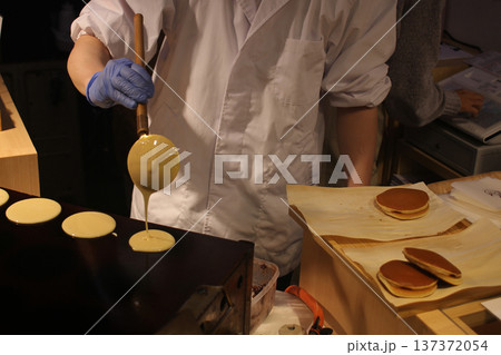 closeup Chef's hands Cooking Japanese Mini Pancakes (Dorayaki batter or castella-style cakes) on Hot Griddle at Food Stall in Sapporo, Japan  137372054