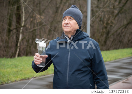 Sporty man drinking water from bottle at public park after workout. Sporty man drinking water from bottle at public park after workout. 137372358