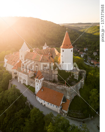 Krivoklat Castle, located in Central Bohemia, displays its medieval charm as the sun sets behind the hills, casting a warm glow over the ancient structure and surrounding landscape. Krivoklat Castle, located in Central Bohemia, displays its medieval charm as the sun sets behind the hills, casting a warm glow over the ancient structure and surrounding landscape. 137373688