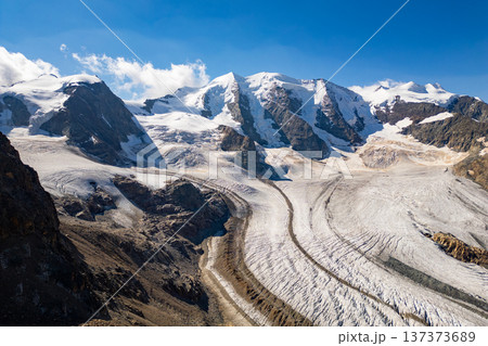 Piz Palu towers high over the Pers Glacier, showcasing the breathtaking beauty of the Swiss Alps. The rocky ridges contrast with the smooth glacier surface under a clear blue sky. 137373689