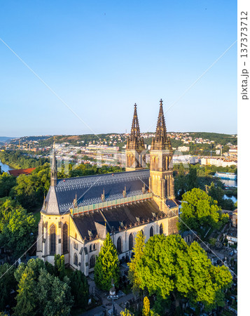 Beneath the clear sky, the Vysehrad Basilica of St. Peter and St. Paul stands majestically in Prague, bathed in warm morning light, revealing the beauty of its architecture and lush surroundings. 137373712
