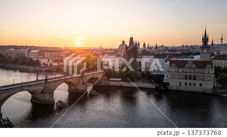 Golden light bathes Charles Bridge in Prague during a peaceful sunrise. The Vltava River reflects the vibrant colors, while historic buildings frame the picturesque view, creating a serene atmosphere. Golden light bathes Charles Bridge in Prague during a peaceful sunrise. The Vltava River reflects the vibrant colors, while historic buildings frame the picturesque view, creating a serene atmosphere. 137373768