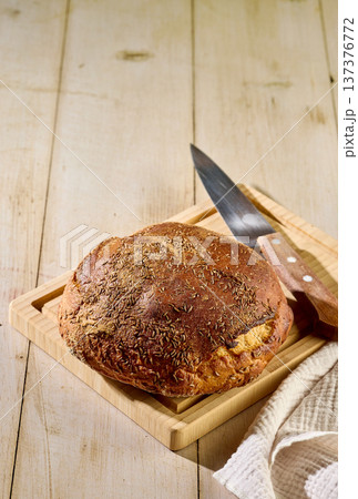 Fresh homemade sweet and sour rye bread with caraway seeds on cutting board with knife on light wooden table Fresh homemade sweet and sour rye bread with caraway seeds on cutting board with knife on light wooden table 137376772
