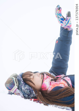 スキーウェアを着てゲレンデで雪と戯れる若い女性 137376904