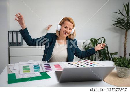 Happy woman enjoying music listening to headphones at office desk Happy woman enjoying music listening to headphones at office desk 137377867