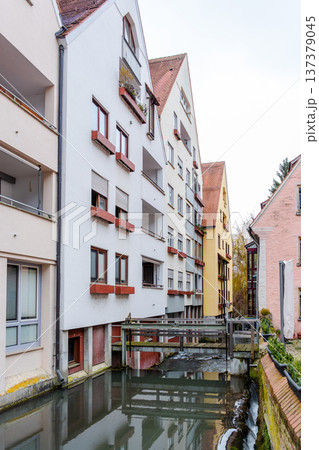 A tranquil canal in the fishermans quarter of Ulm, Germany. Reflections of colorful buildings line the water edge, creating a serene urban scene. 137379045