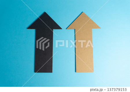 Two arrows made of paper point upward against a blue background showing direction and focus for various purposes or ideas Two arrows made of paper point upward against a blue background showing direction and focus for various purposes or ideas 137379153