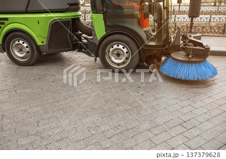 Side view of a green street sweeper machine parked in an urban park area. Side view of a green street sweeper machine parked in an urban park area. 137379628