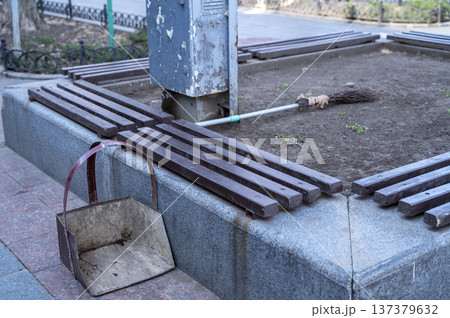 Metal broom and dustpan sitting on a granite curb in a city park Metal broom and dustpan sitting on a granite curb in a city park 137379632