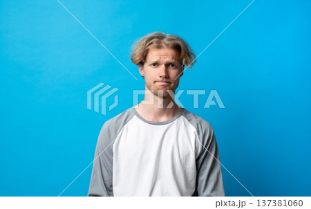 Young man having doubts and feeling uncertain, standing with a skeptical facial expression indicating hesitation, frustration, and disappointment Young man having doubts and feeling uncertain, standing with a skeptical facial expression indicating hesitation, frustration, and disappointment 137381060