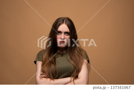 Young woman standing displeased, expressing anger and annoyance with crossed arms against a solid background Young woman standing displeased, expressing anger and annoyance with crossed arms against a solid background 137381067