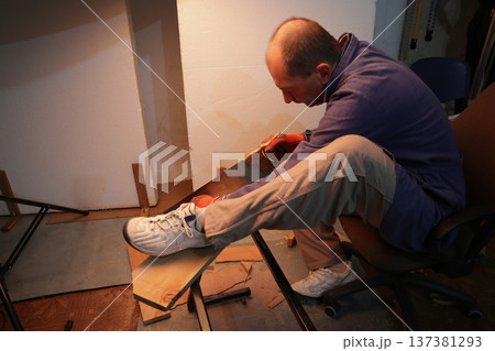 A man saws a board at home on his own. A man saws a board at home on his own. 137381293