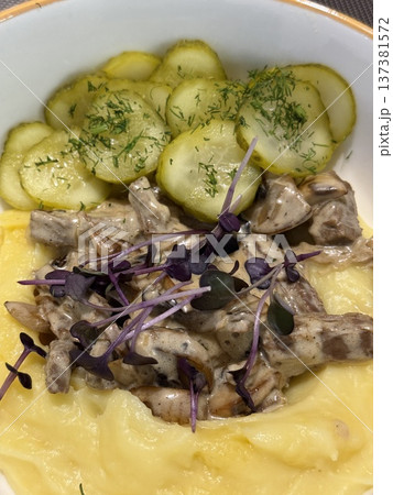 Mashed potatoes with creamy mushroom sauce topped with greens, served with sliced cucumbers Mashed potatoes with creamy mushroom sauce topped with greens, served with sliced cucumbers 137381572