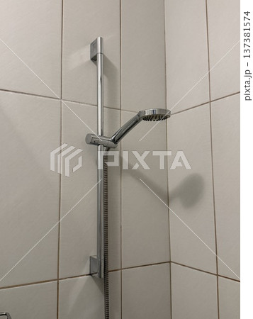 Shower head and hose on tiled bathroom wall with shadow forming a minimalistic background Shower head and hose on tiled bathroom wall with shadow forming a minimalistic background 137381574