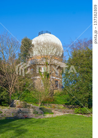 Visitors enjoy the lush green surroundings of the Old Royal Observatory in Greenwich, London, where history and astronomy come together under a clear blue sky. Visitors enjoy the lush green surroundings of the Old Royal Observatory in Greenwich, London, where history and astronomy come together under a clear blue sky. 137382809