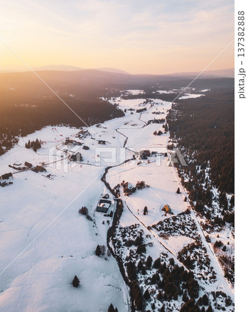 Jizerka mountain village shows snowy landscape from above. Houses are surrounded by white fields and trees. The sunlight creates soft shadows across the land in winter. Jizerka mountain village shows snowy landscape from above. Houses are surrounded by white fields and trees. The sunlight creates soft shadows across the land in winter. 137382888