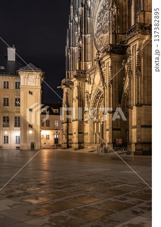 Visitors walk near St Vitus Cathedral at Prague Castle during the night. The historic building is lit up, showing its impressive architecture. The square is quiet and empty. Visitors walk near St Vitus Cathedral at Prague Castle during the night. The historic building is lit up, showing its impressive architecture. The square is quiet and empty. 137382895