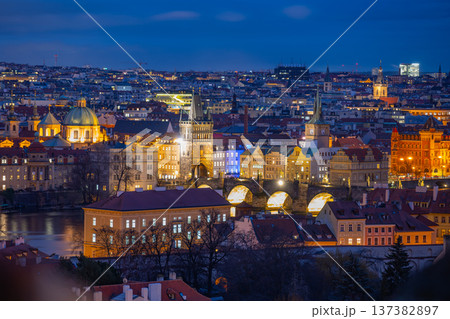 Prague at dusk with buildings and bridges illuminated. The city stretches across the landscape with lights twinkling in the evening sky. 137382897