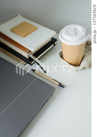 Office table flat lay: laptop, work note pads, pen, takeaway coffee in paper cup. Basic work tools on white table. Corporate job, remote work online. Office table flat lay: laptop, work note pads, pen, takeaway coffee in paper cup. Basic work tools on white table. Corporate job, remote work online. 137383629