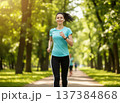 Young attractive woman in a t-shirt and black leggings and wireless earbuds running in the city park outdoor. 137384868