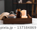 Spa wellness set with reed diffuser, scented candles, pink sea salt and zen stones in a wooden tray on a white towel 137384869