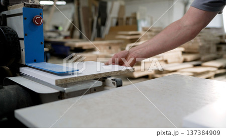 Worker processing a laminated particle board panel on industrial machinery in a furniture workshop. 137384909