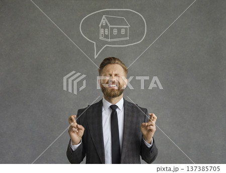 Successful man with a funny expression crosses his fingers dreaming of his own house. Successful man with a funny expression crosses his fingers dreaming of his own house. 137385705