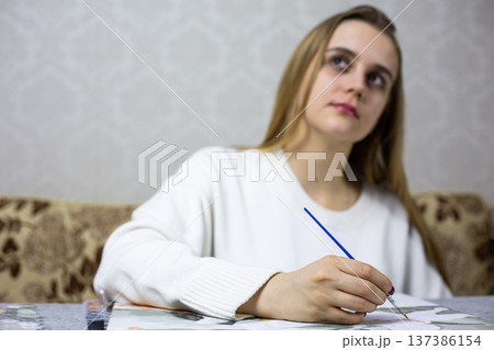 Girl hand with brush paints picture, while head points upward with blurred background. Process of understanding one painting and creative inspiration. Finding ideas for drawing and creativity 137386154