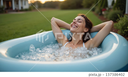 A woman relaxing in a blue inflatable tub filled with ice, set in a green outdoor lawn, enjoying a refreshing moment of wellness. Inflatable Ice Bath Concept For Home 137386402
