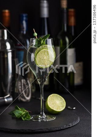 Elegant cocktail Martini Royale garnished with lime slices and fresh mint leaves against a refined bar background with cocktail tools 137386496