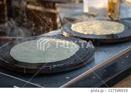 Thin pancakes cooking on round griddle plates with steam rising from hot surface, traditional crepe preparation during Maslenitsa celebration, outdoor food stall. Traditional festival food 137386659