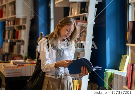 Intelligent woman booklover reading book in cozy bookshop, flipping through pages of publication. Intelligent woman booklover reading book in cozy bookshop, flipping through pages of publication. 137387201