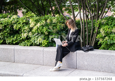 Successful businesswoman working on remote from office in city park using laptop enjoying sunny day. Successful businesswoman working on remote from office in city park using laptop enjoying sunny day. 137387268