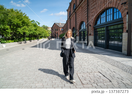 Cheerful businesswoman enjoys walking through summer city street after work day in office. Cheerful businesswoman enjoys walking through summer city street after work day in office. 137387273