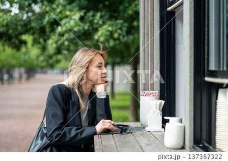 Relaxed businesswoman buying food or coffee at street vendor after productive day in office. Relaxed businesswoman buying food or coffee at street vendor after productive day in office. 137387322