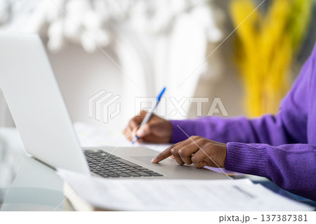 Closeup of Black woman student using laptop, touches touchpad with your finger, makes notes with pen Closeup of Black woman student using laptop, touches touchpad with your finger, makes notes with pen 137387381