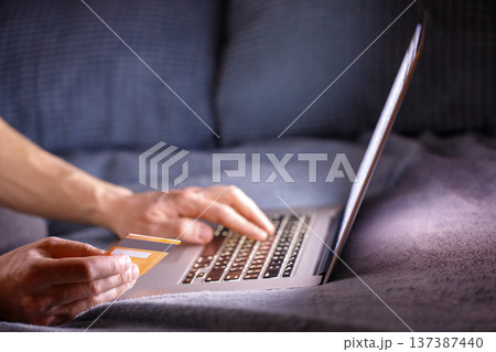 Man hands holding credit card, paying online, sitting on sofa Man hands holding credit card, paying online, sitting on sofa 137387440