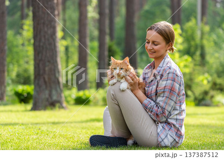 Smiling woman hugging and embracing domestic ginger cat, stroking on head, outdoors in sunny day Smiling woman hugging and embracing domestic ginger cat, stroking on head, outdoors in sunny day 137387512